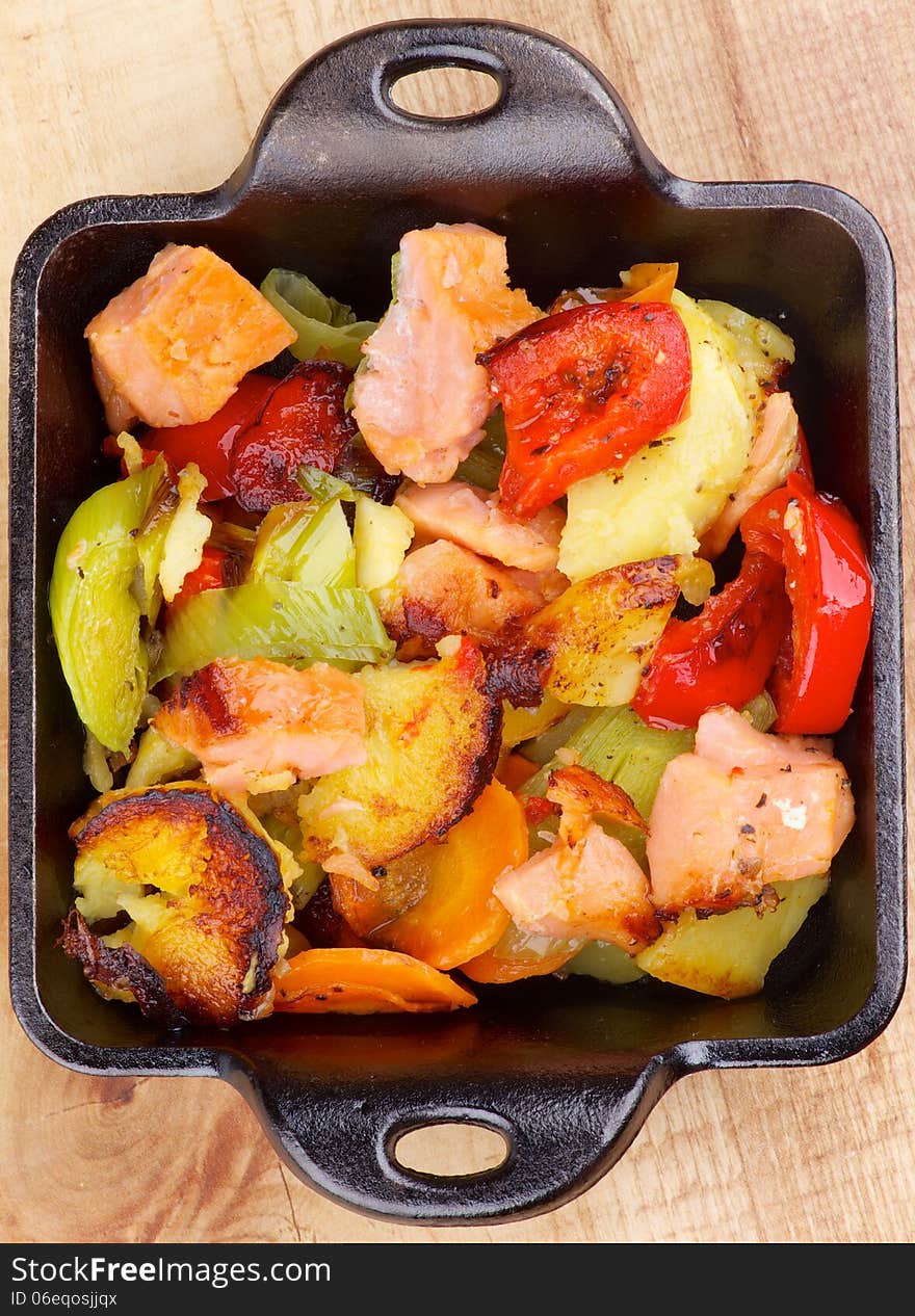 Tasty Homemade Salmon Stew with Potato, Red Bell Pepper, Leek and Carrot in Black Frying Pan on Wooden background. Top View