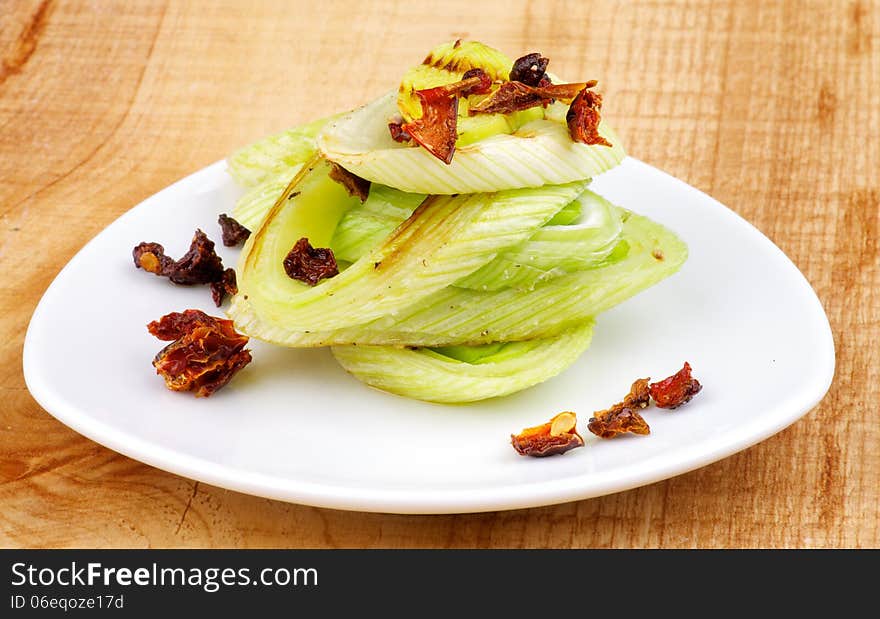 Stack Tasty Roasted Leek with Fried Tomatoes and Paprika on White Plate closeup on Wooden background