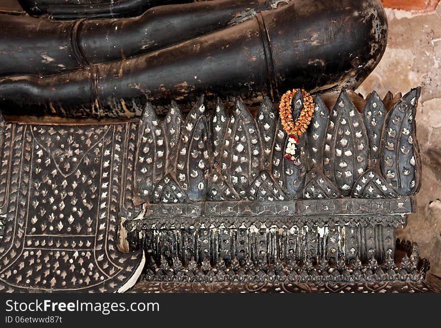 The dried garland hang on the base of black sitting buddha stute in Thailand