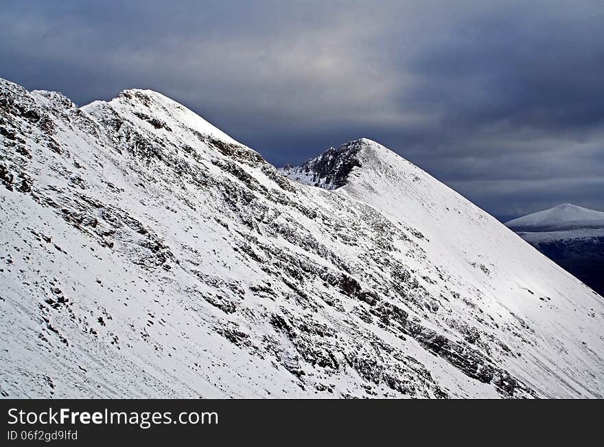 Moody Snow covered Beinn Eighe or Ruadh-stac Mòr, Torridon, Scotland. Beinn Eighe is a long ridge that turns at angles making it a complicated maze of spurs and summits. One of the most popular mountains with mountain walkers and climbers in the Torridon range. Two of its summits are classified as Munros. Moody Snow covered Beinn Eighe or Ruadh-stac Mòr, Torridon, Scotland. Beinn Eighe is a long ridge that turns at angles making it a complicated maze of spurs and summits. One of the most popular mountains with mountain walkers and climbers in the Torridon range. Two of its summits are classified as Munros