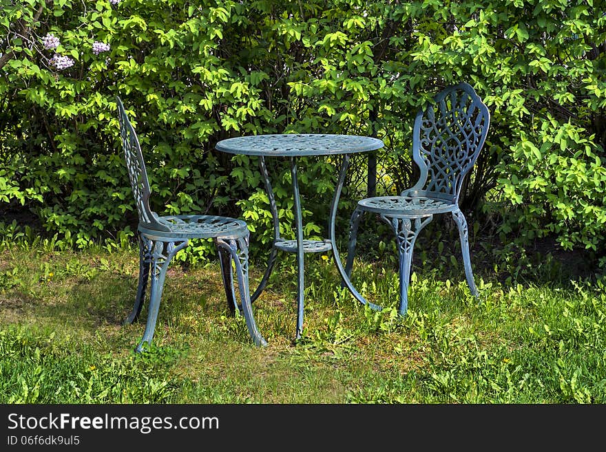 A small green metal table and chairs, are set up and ready for someone to sit and enjoy. A small green metal table and chairs, are set up and ready for someone to sit and enjoy.