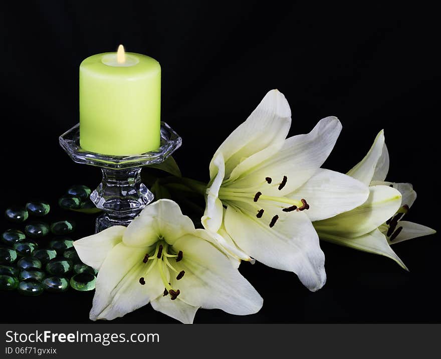 Burning candle and white lilies on a black background