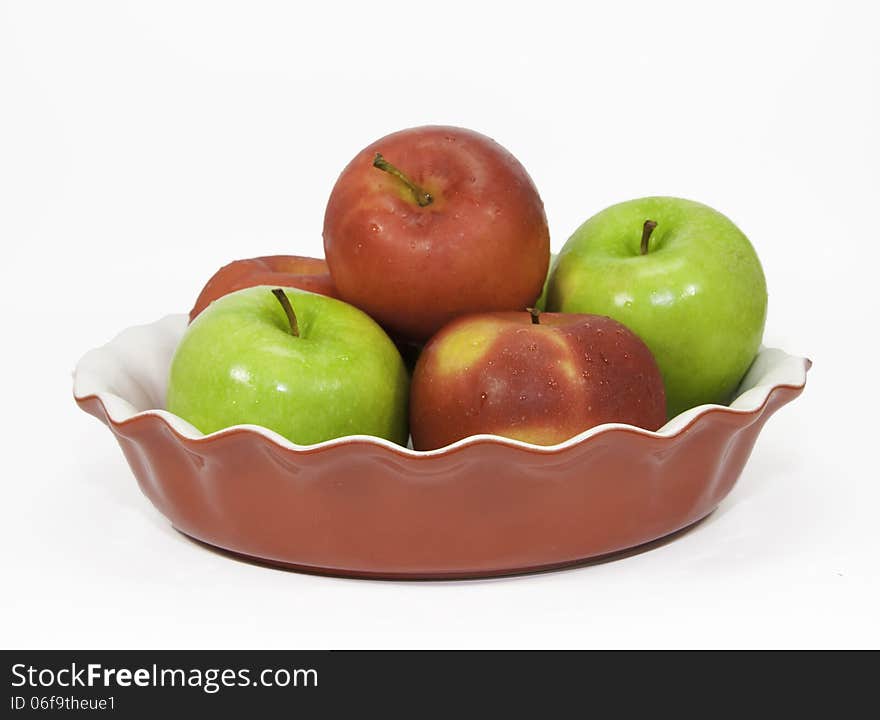 Red and green apples in a red ceramic pie plate against a white background. Red and green apples in a red ceramic pie plate against a white background