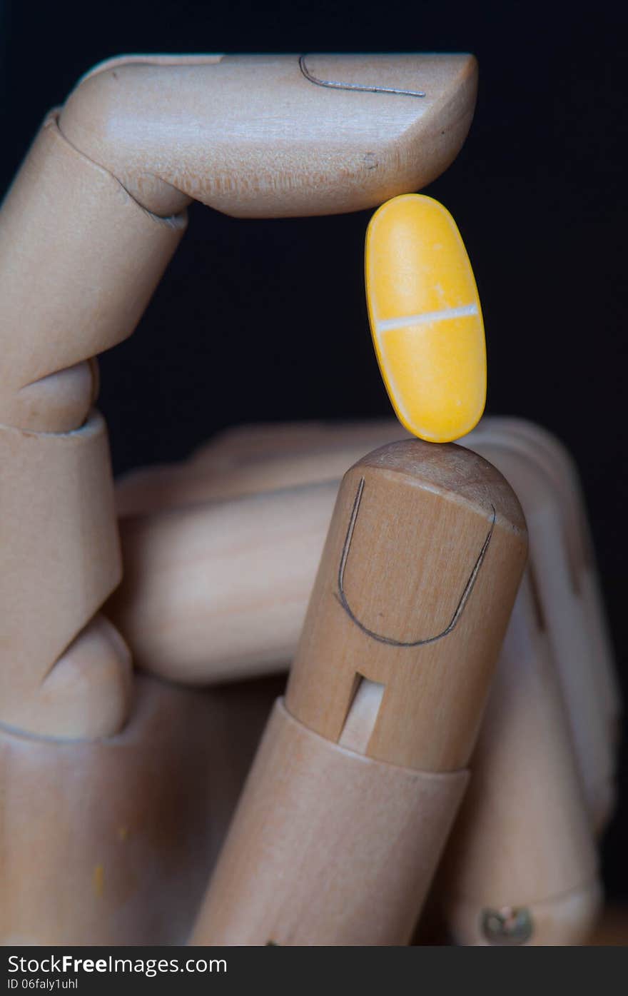 Huge yellow pill between two fingers of a wooden robot like hand.