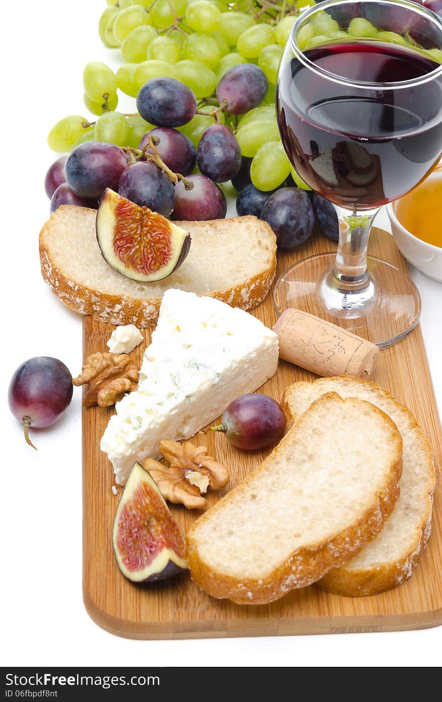 Snacks - cheese, bread, figs, grapes, nuts and red wine on a wooden board isolated on white