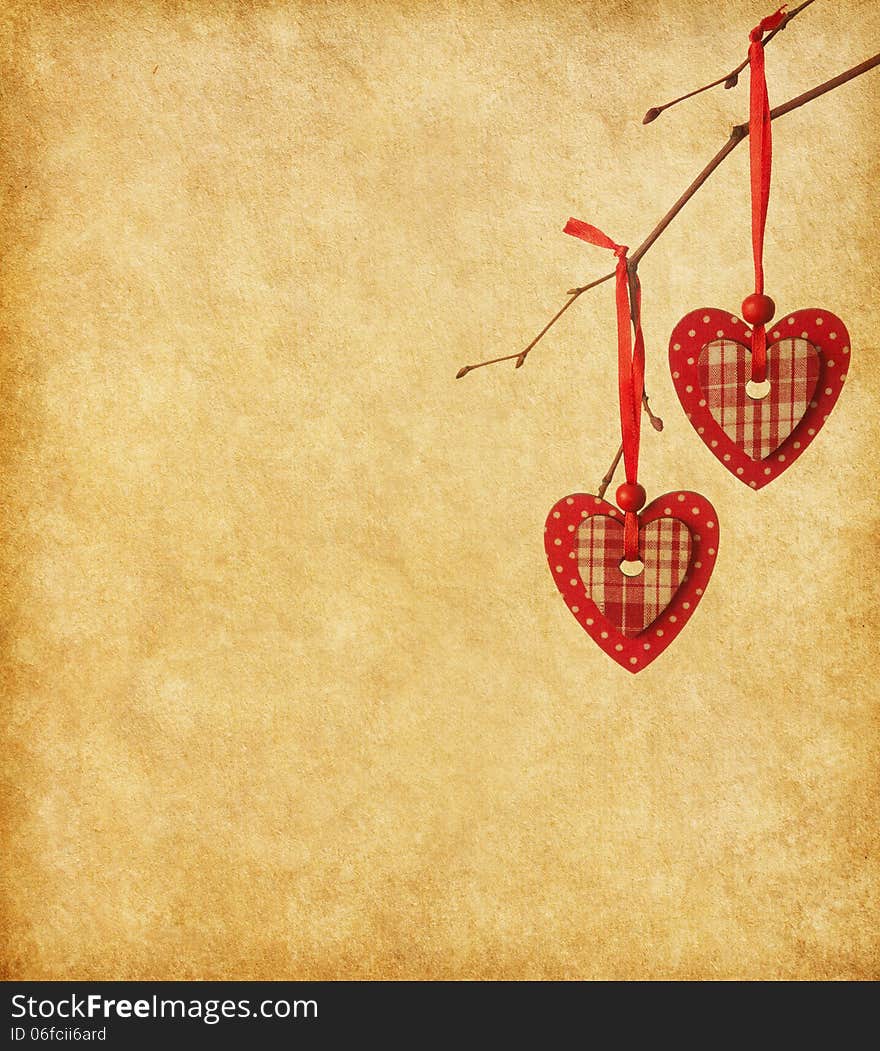 Two red hearts, hanging on a branch over the paper background.