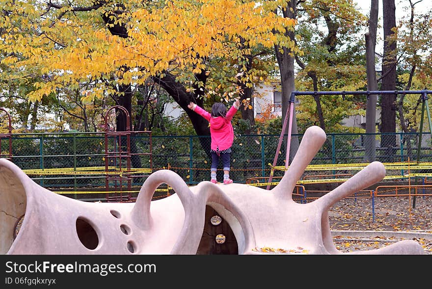 Cute child playing with autumn leafs in playground