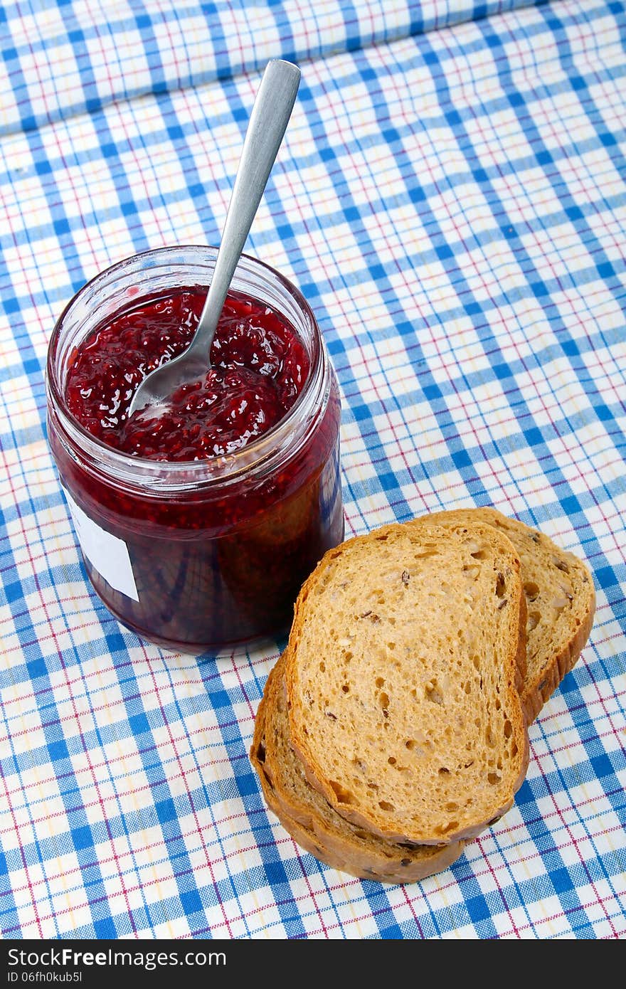 Bread and jar with raspberry jam on blue tablecloth