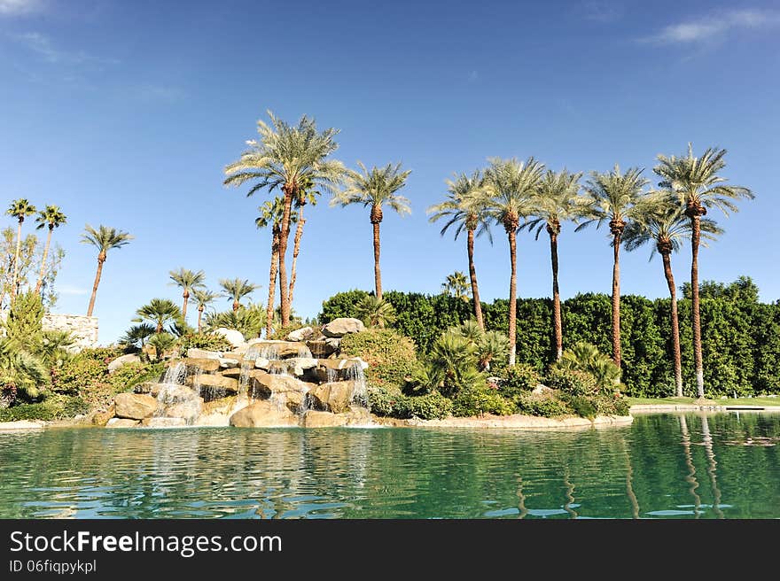 Fountain of water over boulders with row of palm trees. Fountain of water over boulders with row of palm trees