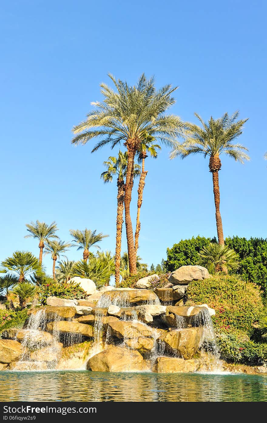 Fountain of water over boulders with row of palm trees. Fountain of water over boulders with row of palm trees