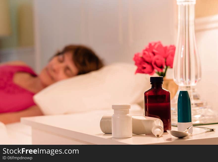 Lady sick in bed with medications sitting on the night table