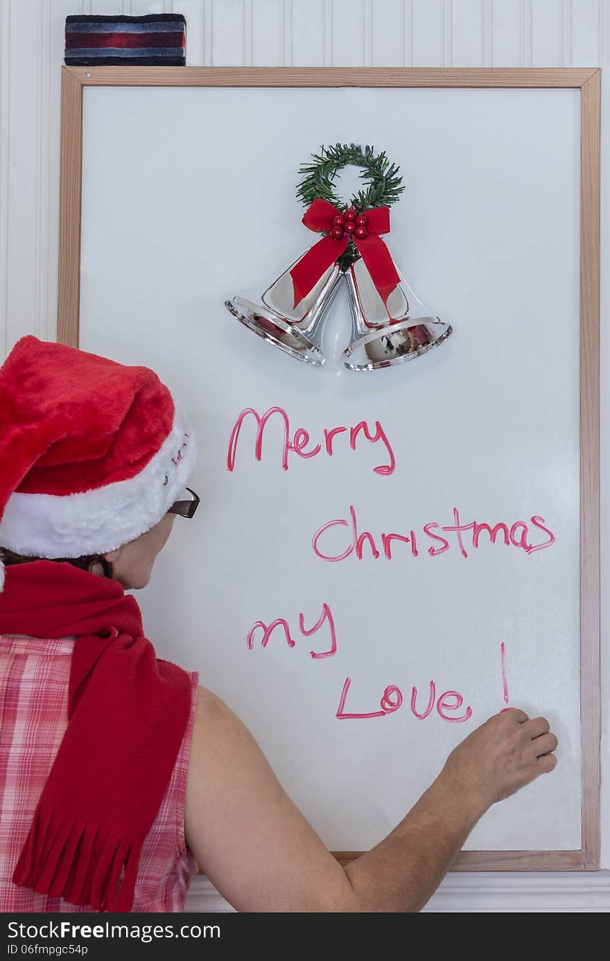 Lady in Santa hat and red scarf writing a christmas message on white board. Lady in Santa hat and red scarf writing a christmas message on white board