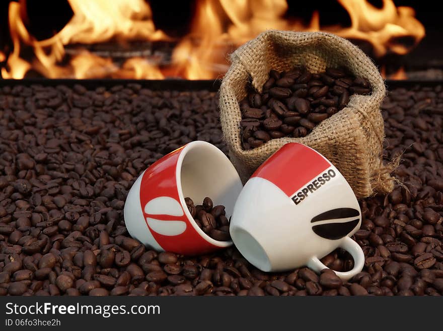 Two ceramic cups and a jute sack with coffee beans on a background of fire. Two ceramic cups and a jute sack with coffee beans on a background of fire