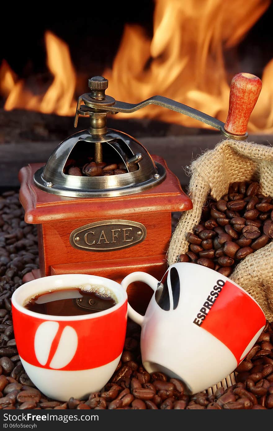 Two ceramic cups, jute sack with coffee beans and coffee grinder on a background of fire. Two ceramic cups, jute sack with coffee beans and coffee grinder on a background of fire