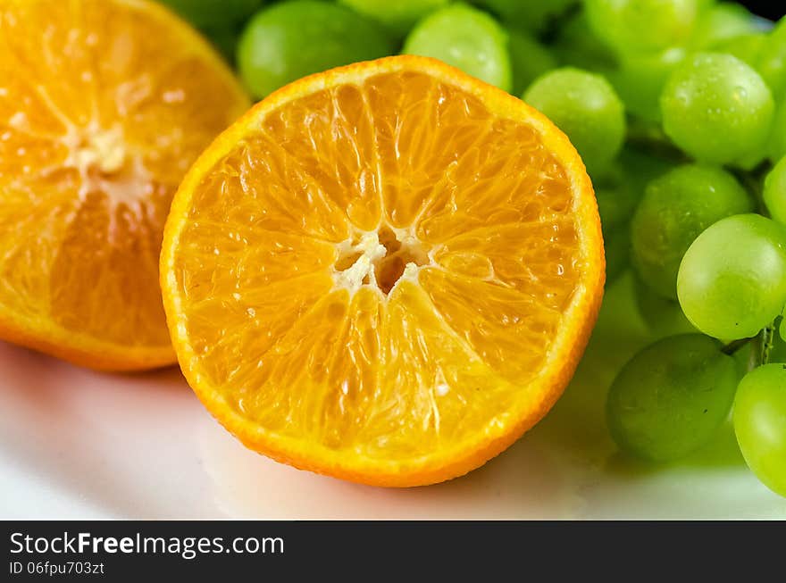 Pink grapefruit sliced in half with green grapes in the background.