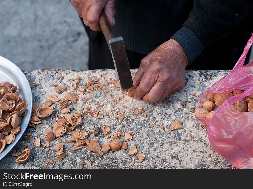 Senior woman is breaking almonds with a metal hammer. Senior woman is breaking almonds with a metal hammer.