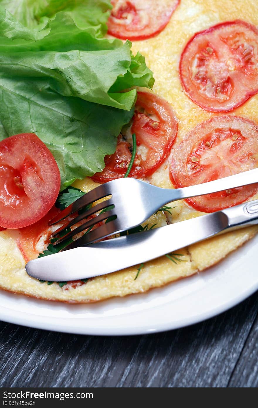 Closeup of fork and knife on plate with omelet and tomatoes. Closeup of fork and knife on plate with omelet and tomatoes