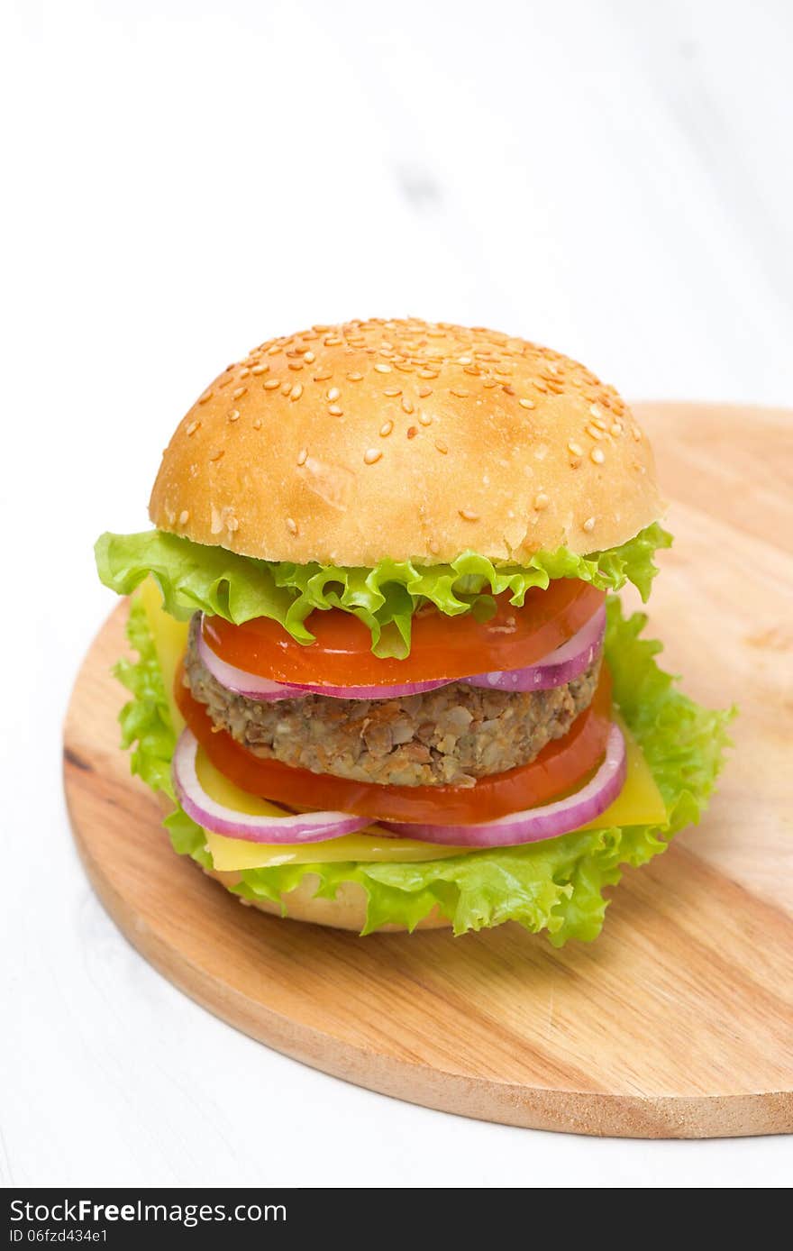 Burger with a vegetarian cutlet and fresh vegetables on wooden board, vertical