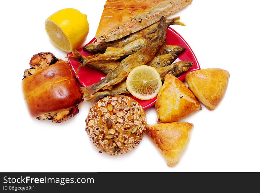 A piece of a fish pie, cakes with lemon, bread, fried fish on red original plate and lemon. Picturesque still life on a stand-alone background. A piece of a fish pie, cakes with lemon, bread, fried fish on red original plate and lemon. Picturesque still life on a stand-alone background.