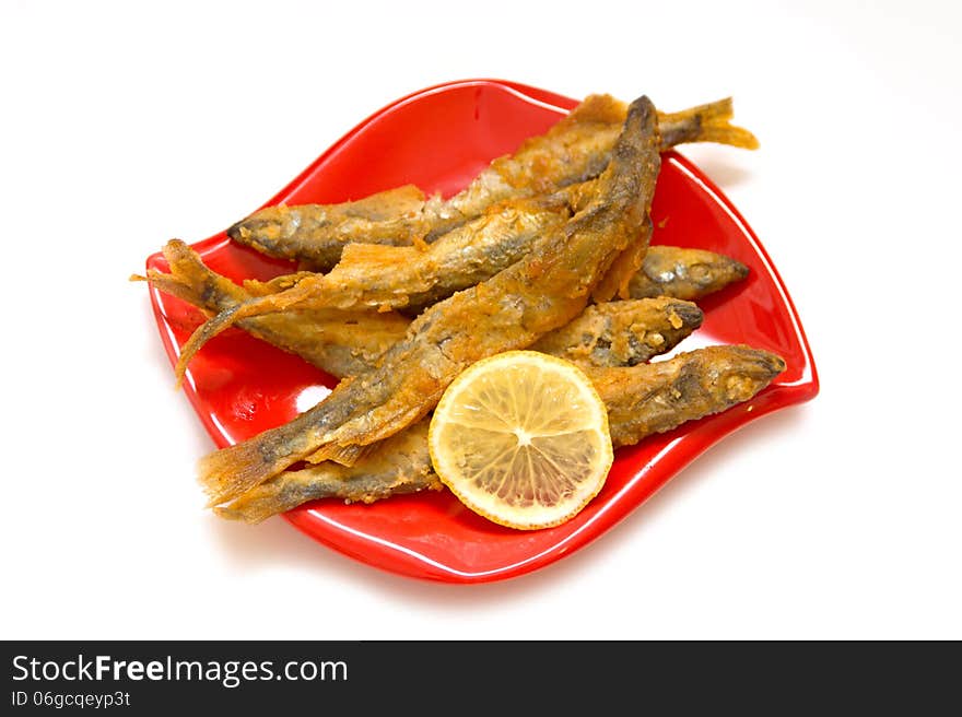 Fried fish and lemon on a red plate, isolated background. Fried fish and lemon on a red plate, isolated background