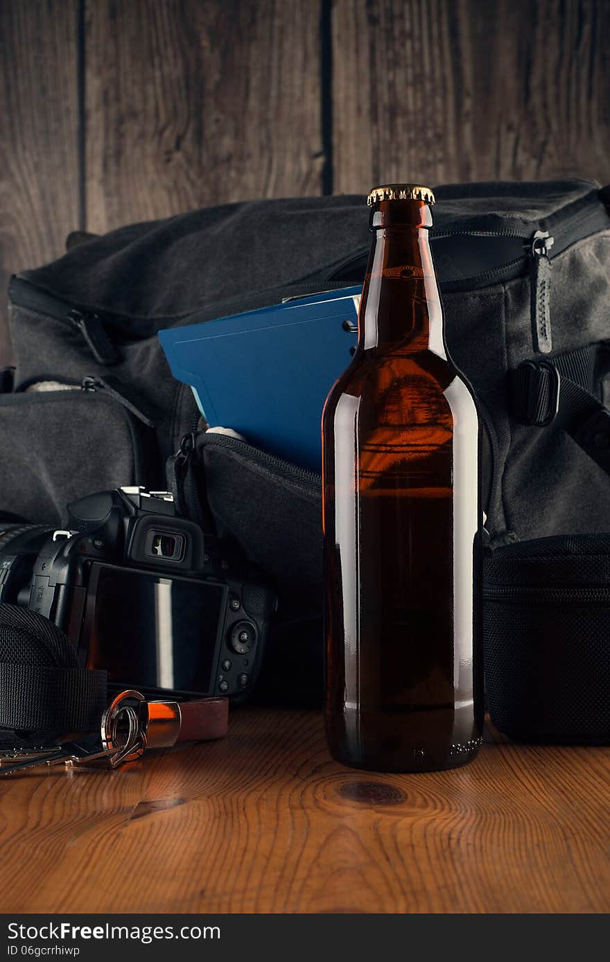 Bottle of beer in the background of several items. Photocamera, coach bag, notebook, keys, wooden table. Bottle of beer in the background of several items. Photocamera, coach bag, notebook, keys, wooden table.