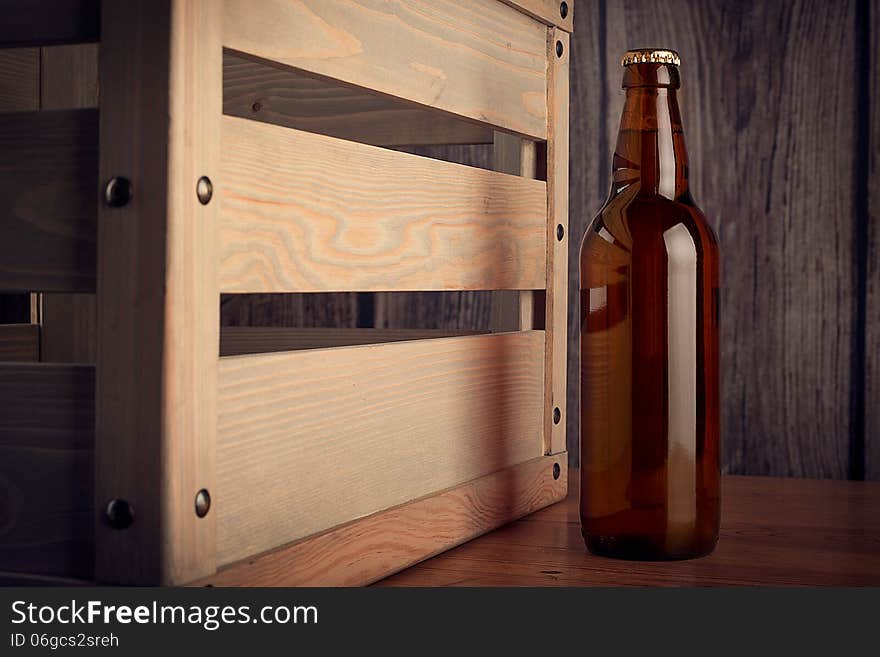 Image of a bottle of beer next to a wooden box on wooden background.