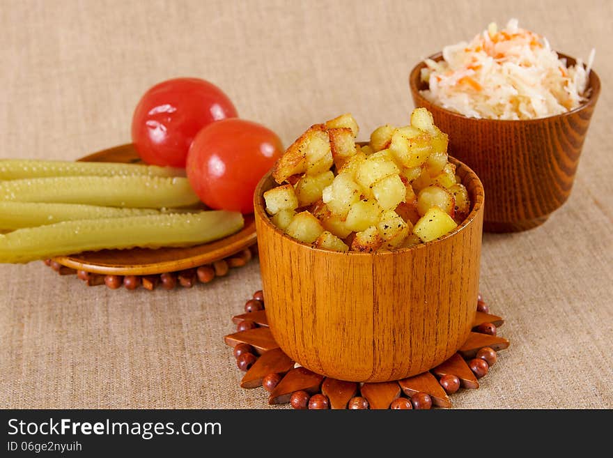 Fried potato cubes with sour cabbage and pickle in a wooden bowl. Fried potato cubes with sour cabbage and pickle in a wooden bowl