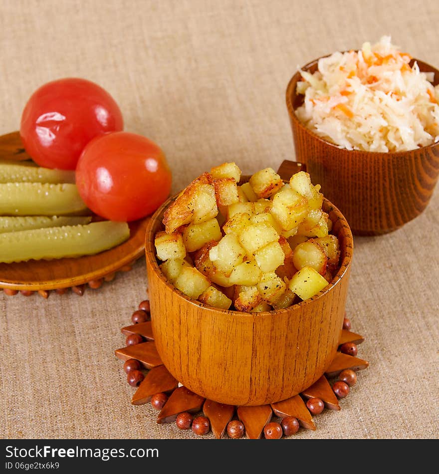 Fried potato cubes with sour cabbage and pickle in a wooden bowl. Fried potato cubes with sour cabbage and pickle in a wooden bowl