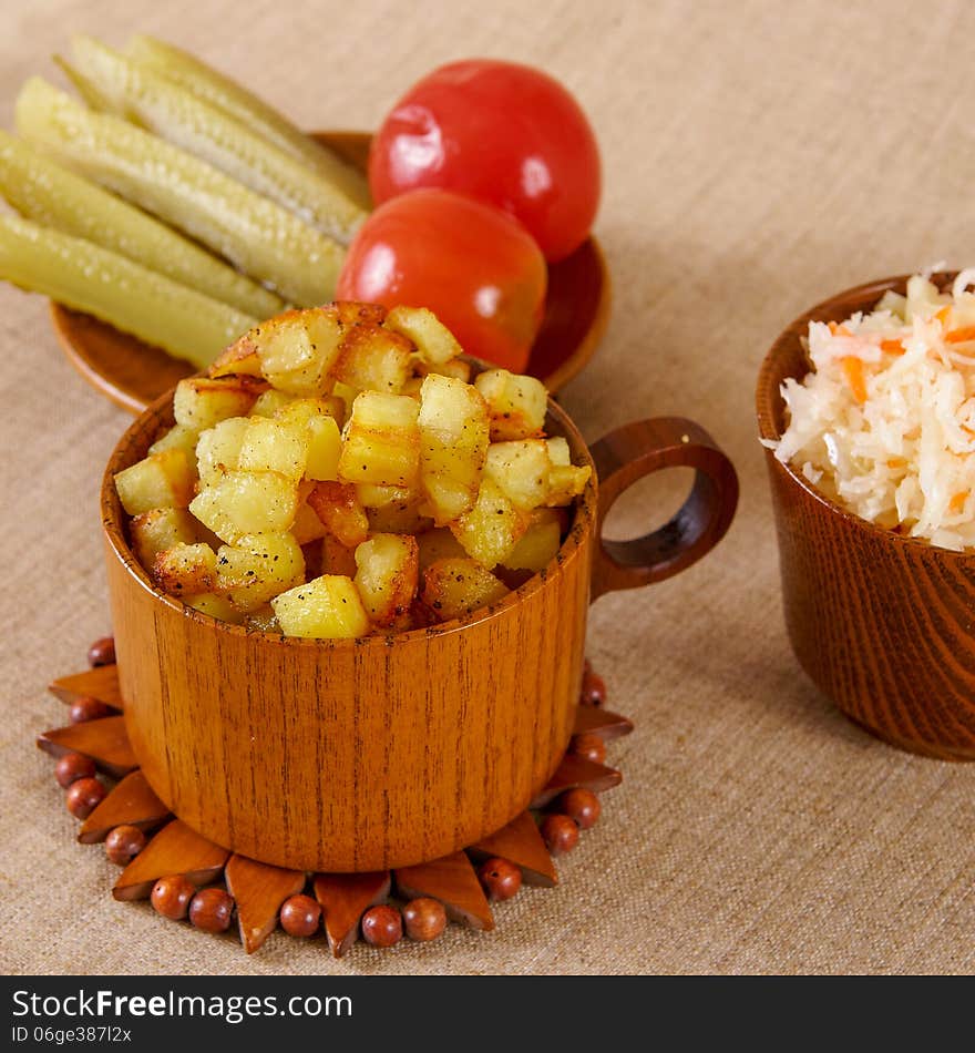 Fried potato cubes with sour cabbage and pickle in a wooden bowl. Fried potato cubes with sour cabbage and pickle in a wooden bowl