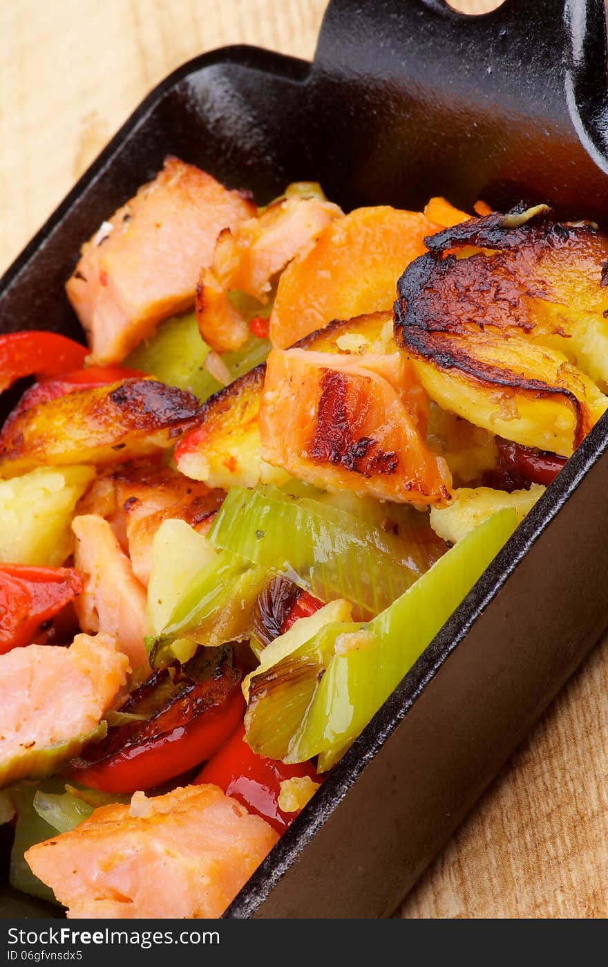 Homemade Salmon Stew with Potato, Red Bell Pepper, Leek and Carrot in Black Frying Pan closeup on Wooden background