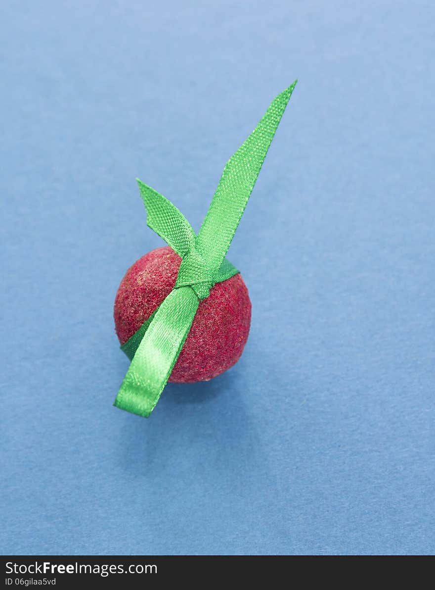 Red shoko praline with green ribbon on blue background