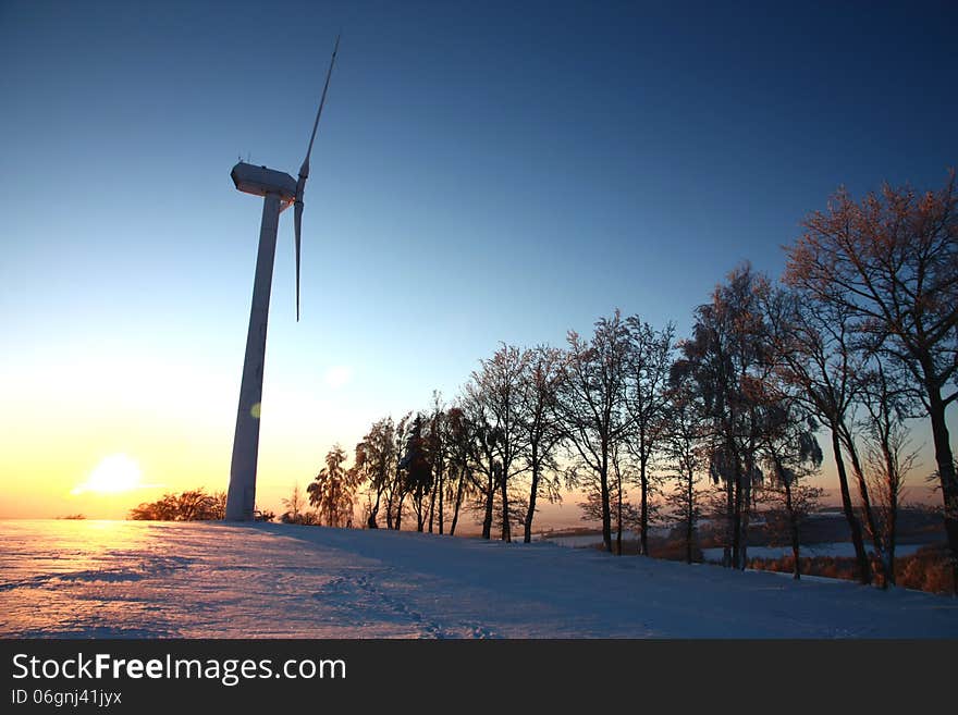 Mast wind turbine in a winter landscape, setting sun and wind power