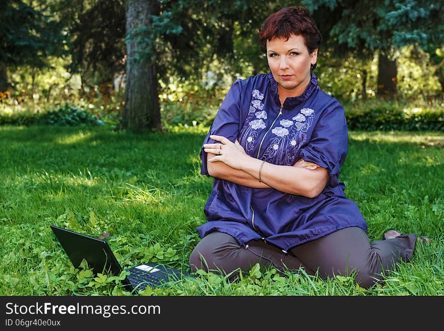 Beautiful woman sitting cross-legged with her laptop on her lap on a green lawn. Beautiful woman sitting cross-legged with her laptop on her lap on a green lawn.