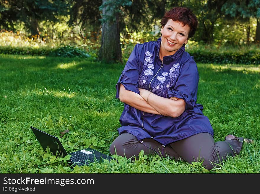 Beautiful woman sitting cross-legged with her laptop on her lap on a green lawn. Beautiful woman sitting cross-legged with her laptop on her lap on a green lawn.