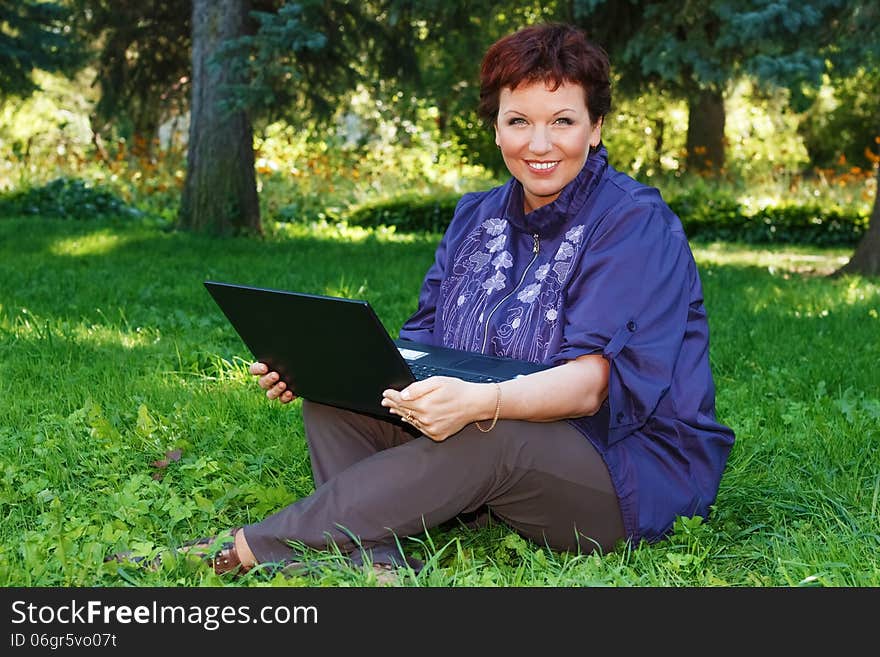 Beautiful woman sitting cross-legged with her laptop on her lap on a green lawn. Beautiful woman sitting cross-legged with her laptop on her lap on a green lawn.