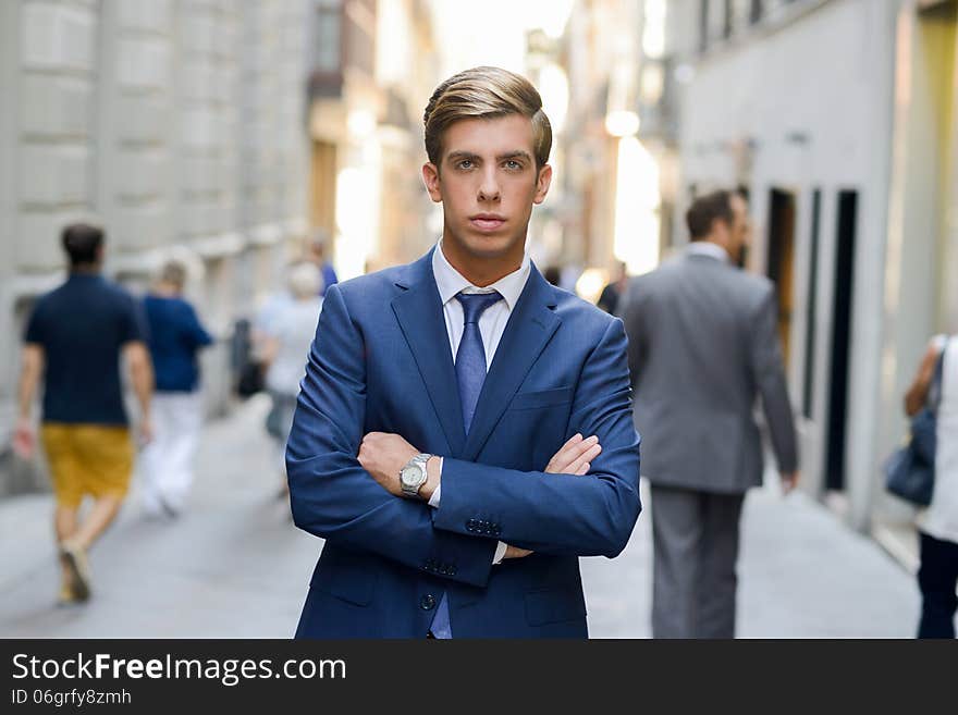 Portrait of an attractive young businessman in urban background wearing blue suit a necktie. Blonde hair