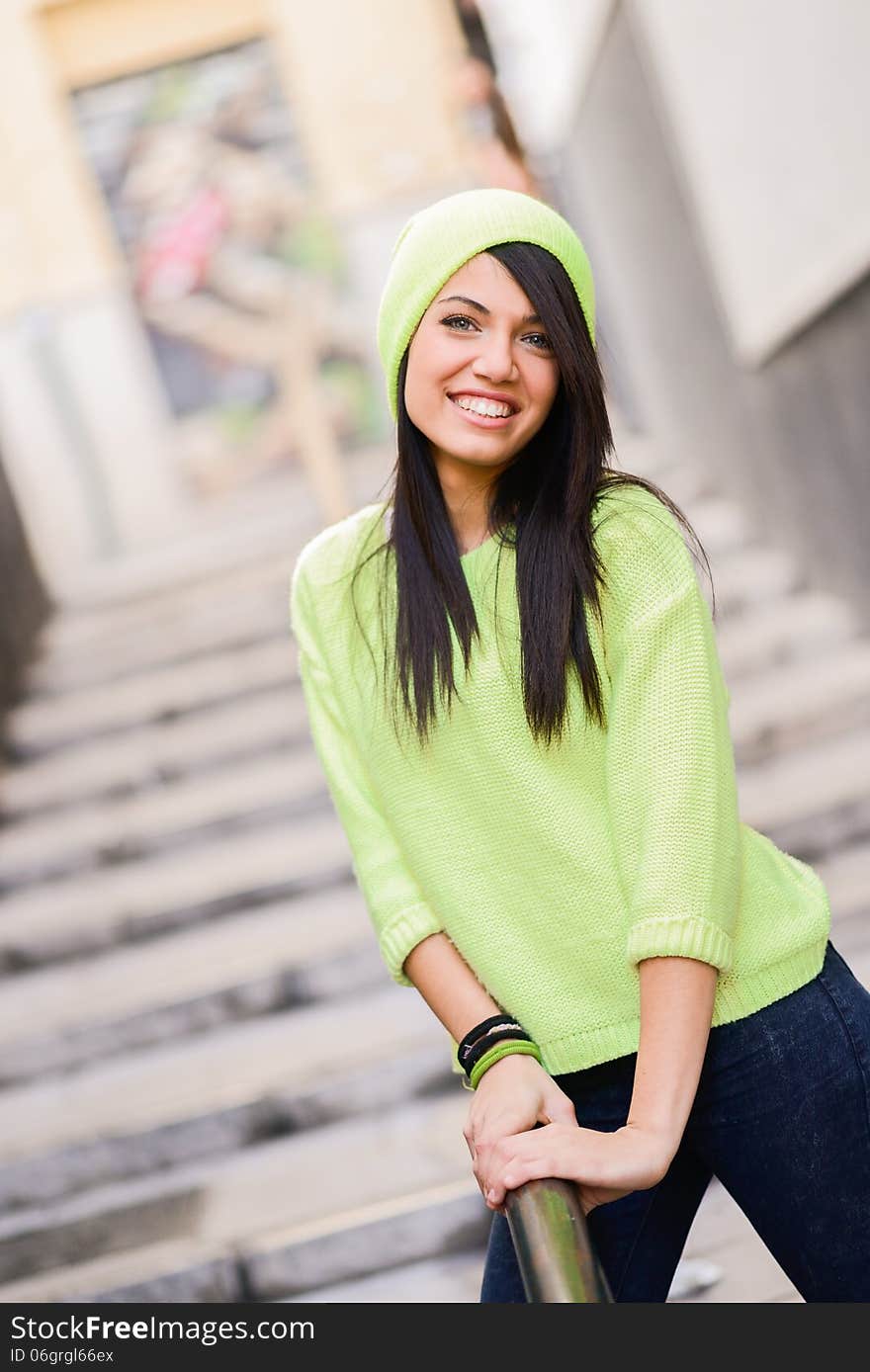 Portrait of brunette young woman with green eyes, wearing green casual clothes and hat, in urban background. Portrait of brunette young woman with green eyes, wearing green casual clothes and hat, in urban background