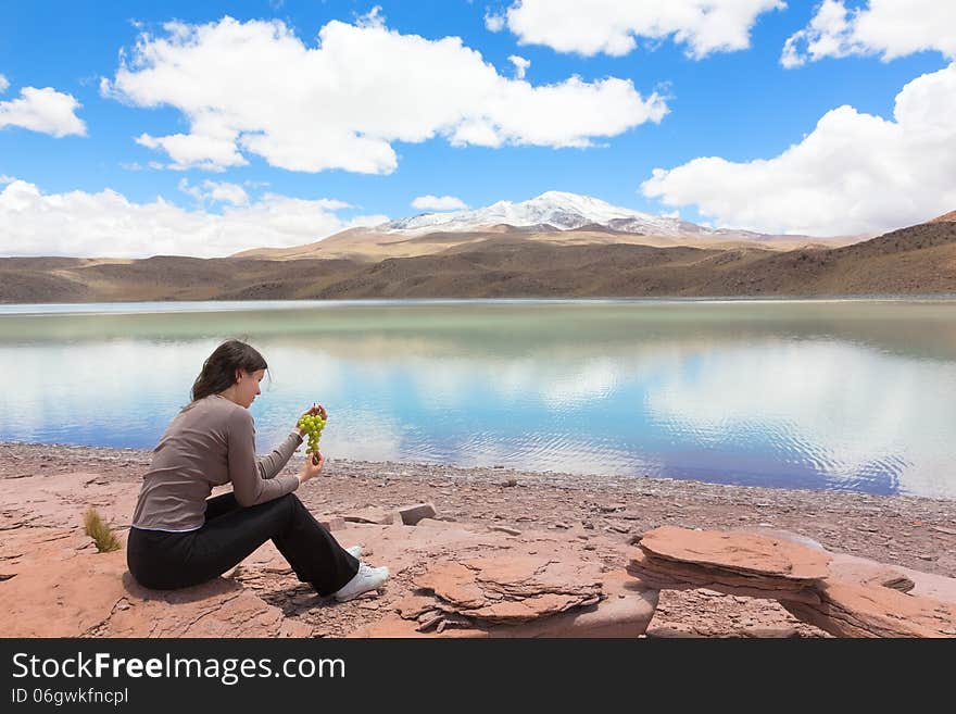 Woman sitting at the shore of lagoon Celeste, Bolivia and eating grape. Woman sitting at the shore of lagoon Celeste, Bolivia and eating grape