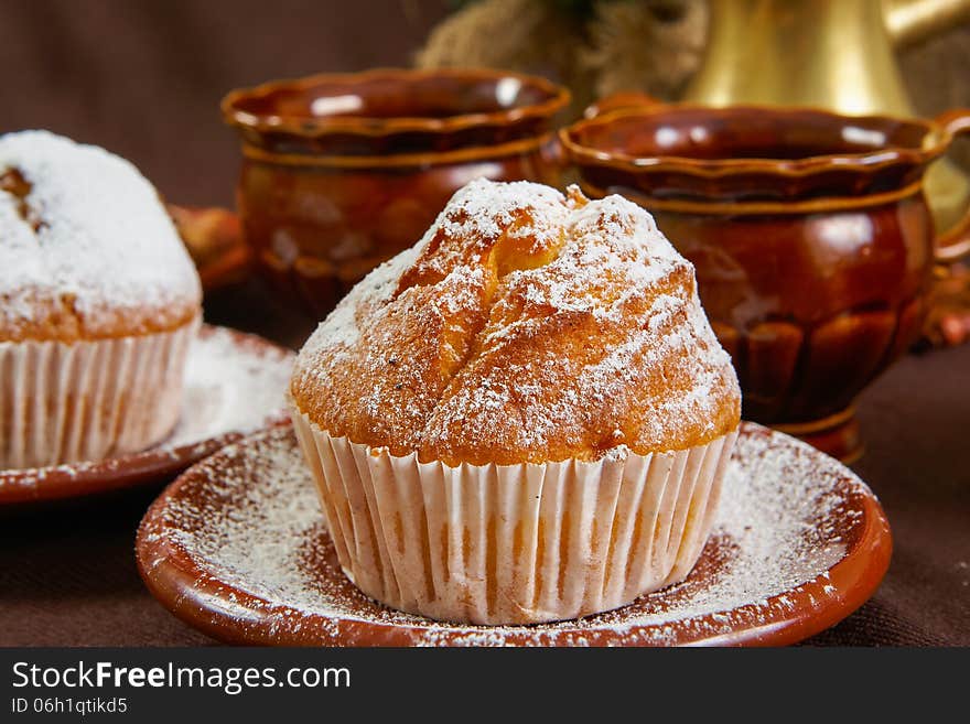 Fresh muffins on a brown table with a cups of coffee and coffee pot