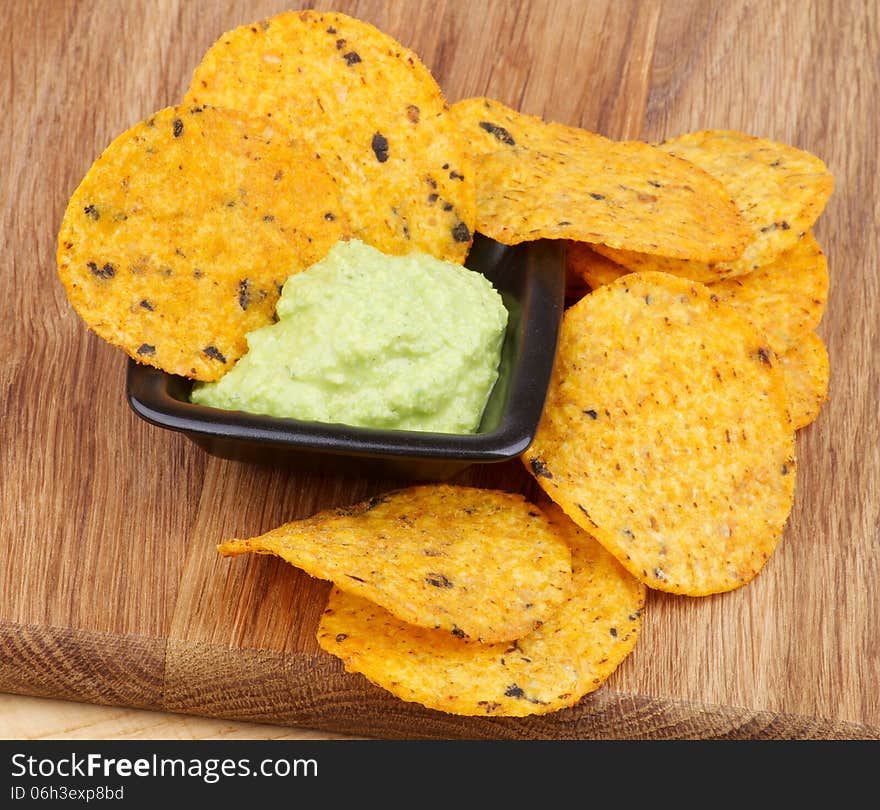 Arrangement of Tortilla Chips and Guacamole Sauce in Black Bowl closeup on Wooden Board