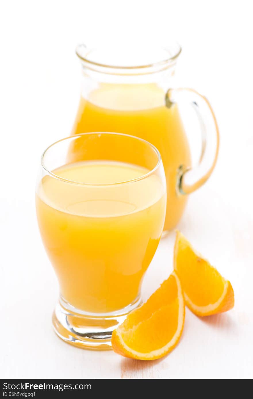 Glass and jug of orange juice and fresh orange slices, vertical