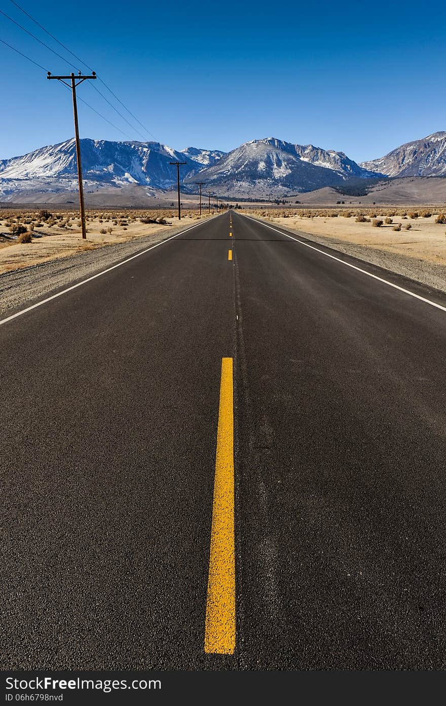 Single yellow line in middle of road leading to the mountains with telephone poles on one side. Single yellow line in middle of road leading to the mountains with telephone poles on one side