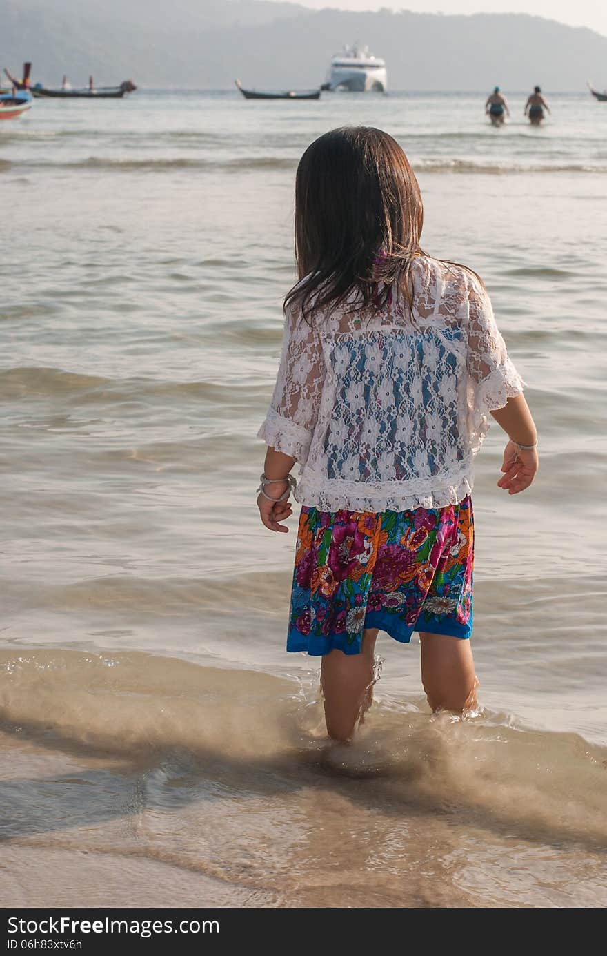 Backview of a caucasian white girl child with long blond hair standing and playing in the water of the Phuket on a beach in Thailand during summer holidays. Backview of a caucasian white girl child with long blond hair standing and playing in the water of the Phuket on a beach in Thailand during summer holidays.