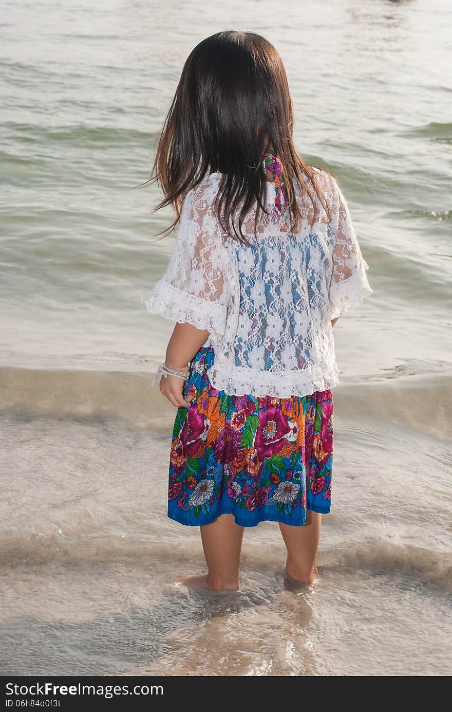 Backview of a caucasian white girl child with long blond hair standing and playing in the water of the Phuket on a beach in Thailand during summer holidays. Backview of a caucasian white girl child with long blond hair standing and playing in the water of the Phuket on a beach in Thailand during summer holidays.