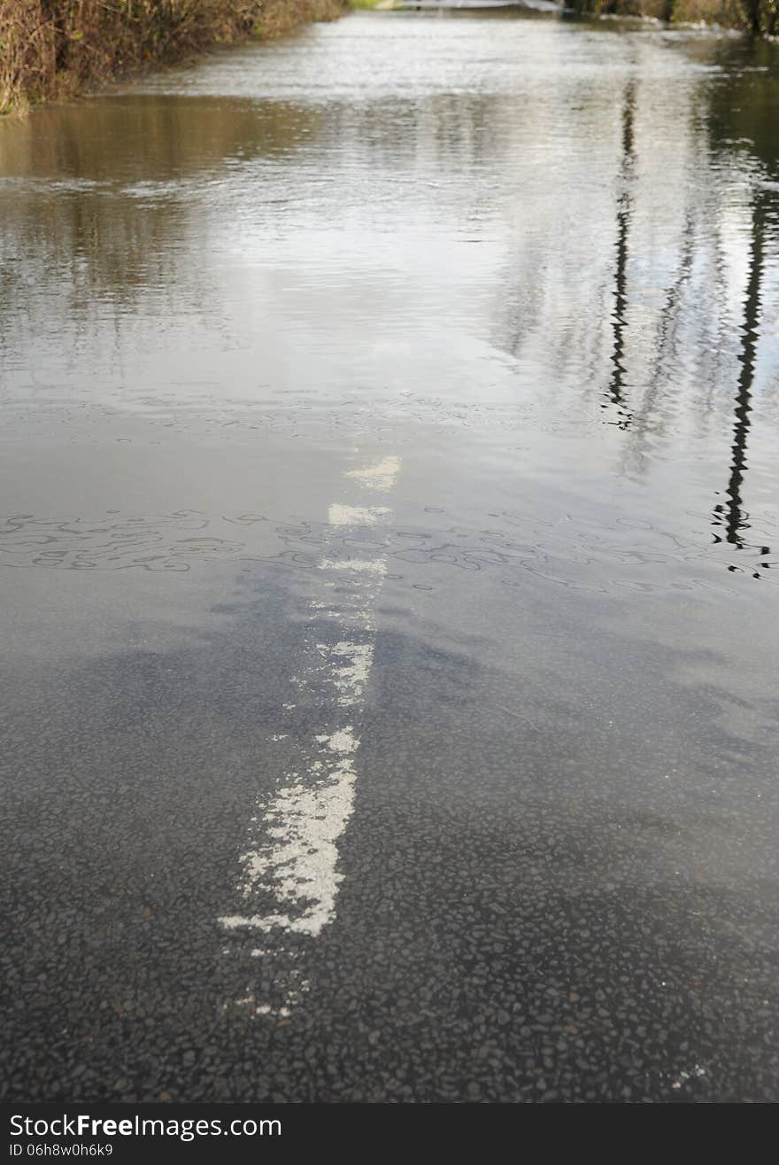 A country road is closed as a swollen river breaks its banks. Hampshire, England UK Low perspective, reflections, submerged road marking. A country road is closed as a swollen river breaks its banks. Hampshire, England UK Low perspective, reflections, submerged road marking.