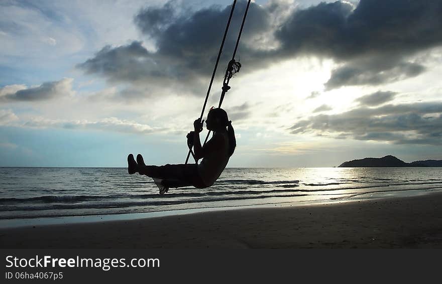Woman's silhouette on a swing at the beach.