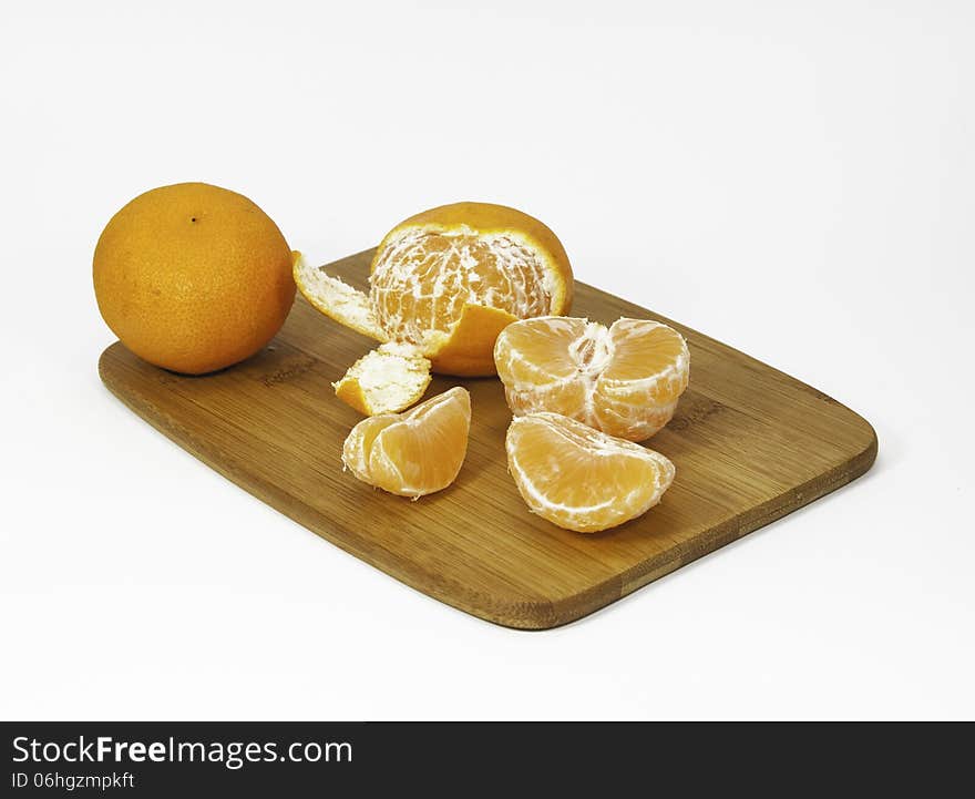 Clementine oranges, peeled and unpeeled, on a bamboo cutting board against a white background. Clementine oranges, peeled and unpeeled, on a bamboo cutting board against a white background