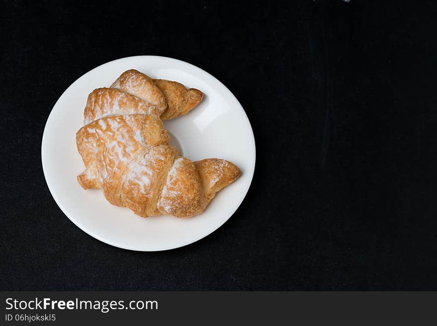 Fresh croissant on a plate on black background, top view