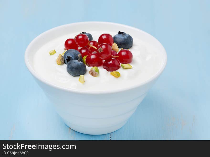 Fresh sweet yogurt with berries and pistachios in bowl, closeup