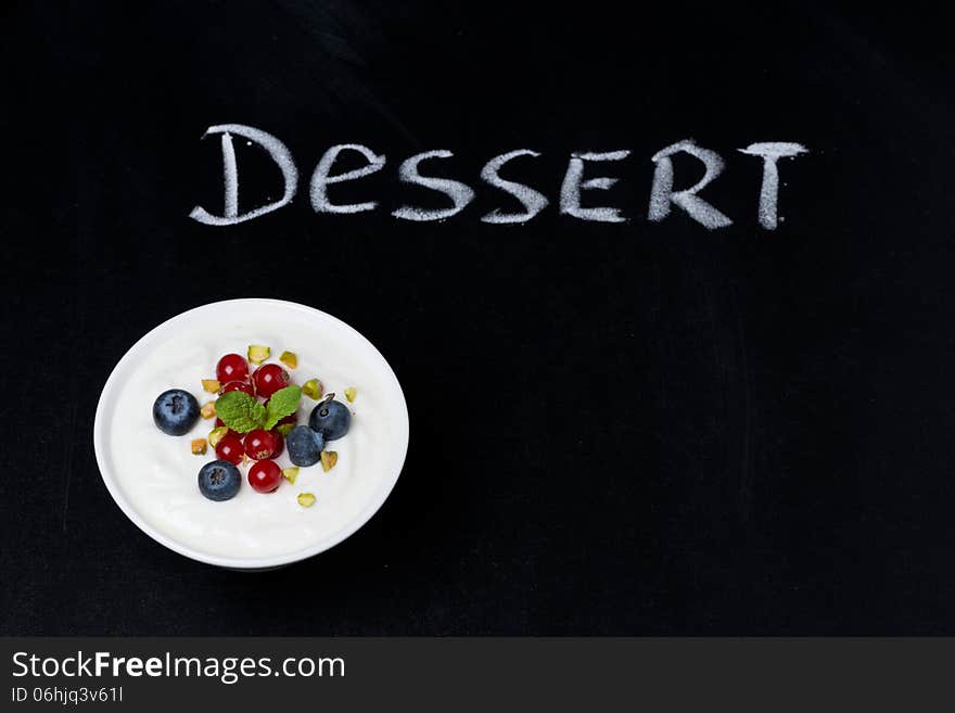 Yogurt with fresh berries on a black background and the word dessert written in chalk, top view, horizontal. Yogurt with fresh berries on a black background and the word dessert written in chalk, top view, horizontal